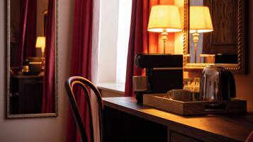 A hotel room with a wooden desk, a chair, a mirror, and a window with red curtains.
