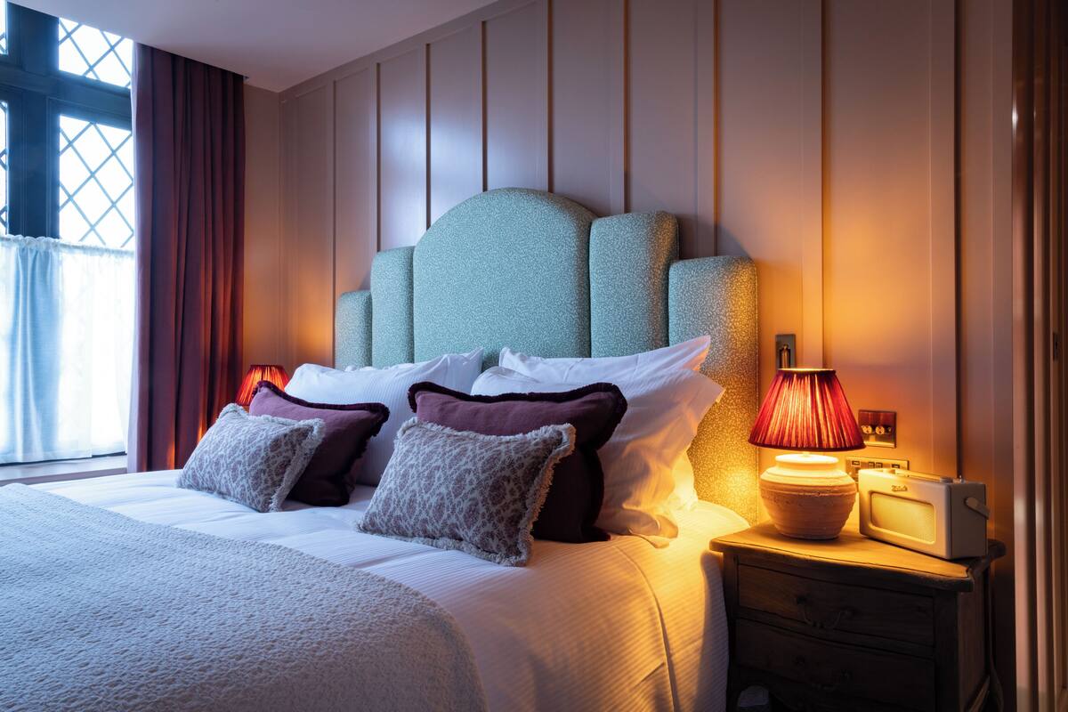 A neatly made bed with a headboard, pillows, a bedside lamp, and a radio on a nightstand.