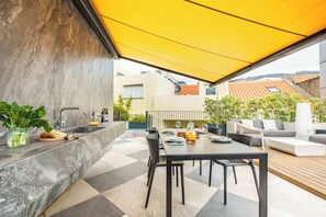 Un espace extérieur aménagé pour les repas, avec une table et des chaises, un évier intégré et un auvent jaune.