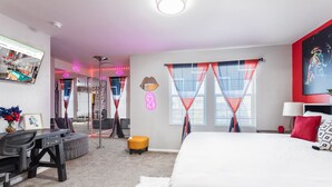 A modern hotel room with a large bed, a desk, and a chair. There is a window with curtains and a painting on the wall. - 420Friendly Game Arcade DancePole Airport DIA (Denver)