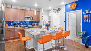 A modern kitchen with wooden cabinets, a central island with bar stools, and a blue accent wall. - 420Friendly Game Arcade DancePole Airport DIA (Denver)
