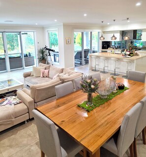 A spacious living area with a wooden dining table, beige sofas, and a kitchen in the background.