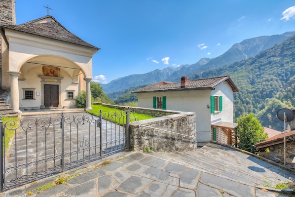 A stone building with a balcony, a gate, and a mountain backdrop.