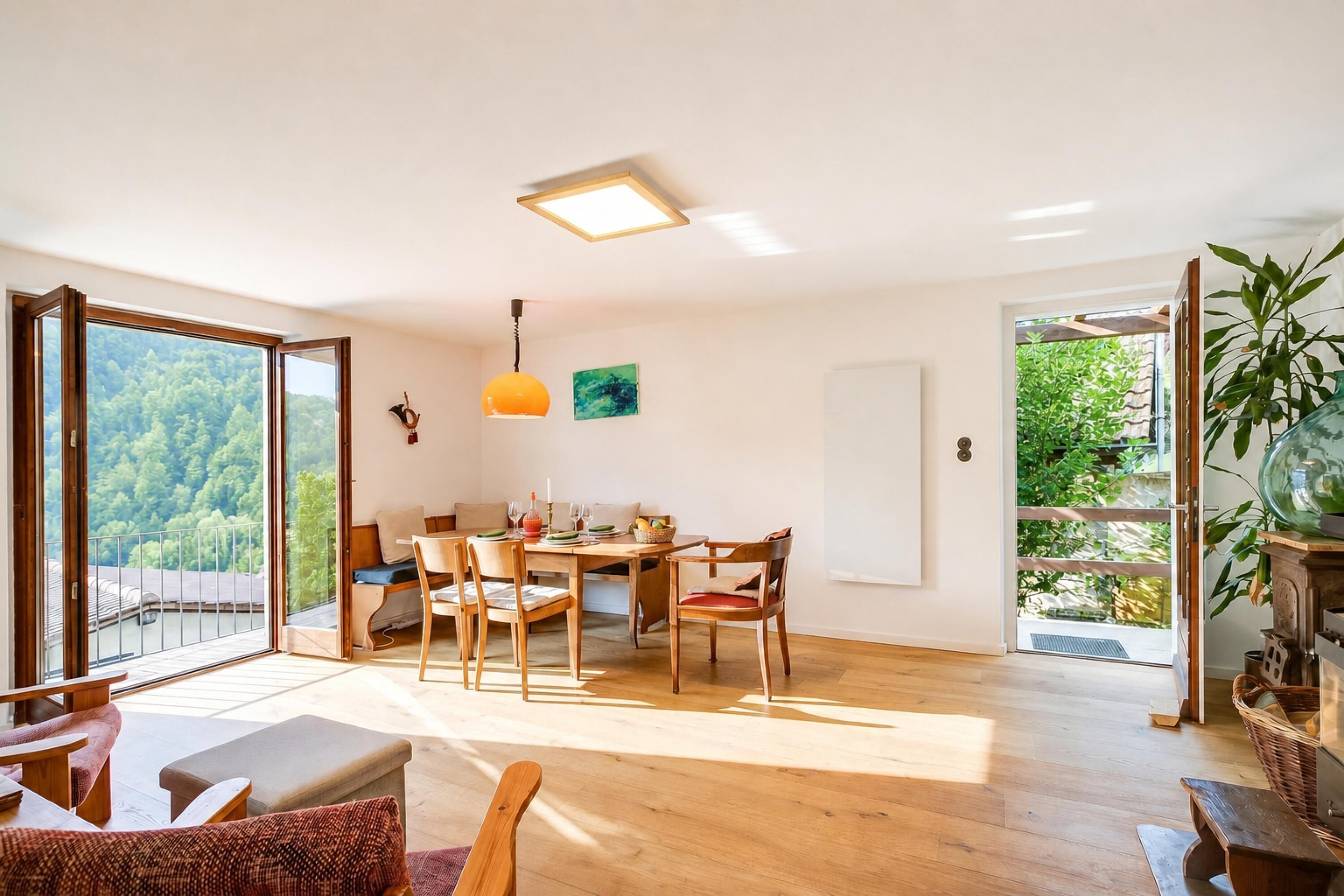 A spacious room with a dining area, a large window with a view of greenery, and a ceiling light fixture.