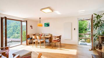 A spacious room with a dining area, a large window with a view of greenery, and a ceiling light fixture.
