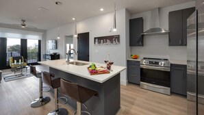 A modern kitchen with a central island, stainless steel appliances, and a dining area with bar stools. - West End Getaway for 5 w/Pool! (Nashville)