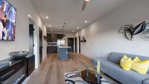 A modern living room with a grey sofa, yellow cushions, a glass coffee table, and a TV displaying a band. - West End Getaway for 5 w/Pool! (Nashville)