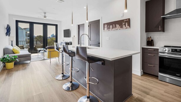 A modern kitchen with a central island, bar stools, and a dining area with a sofa and chairs. - West End Getaway for 5 w/Pool! (Nashville)