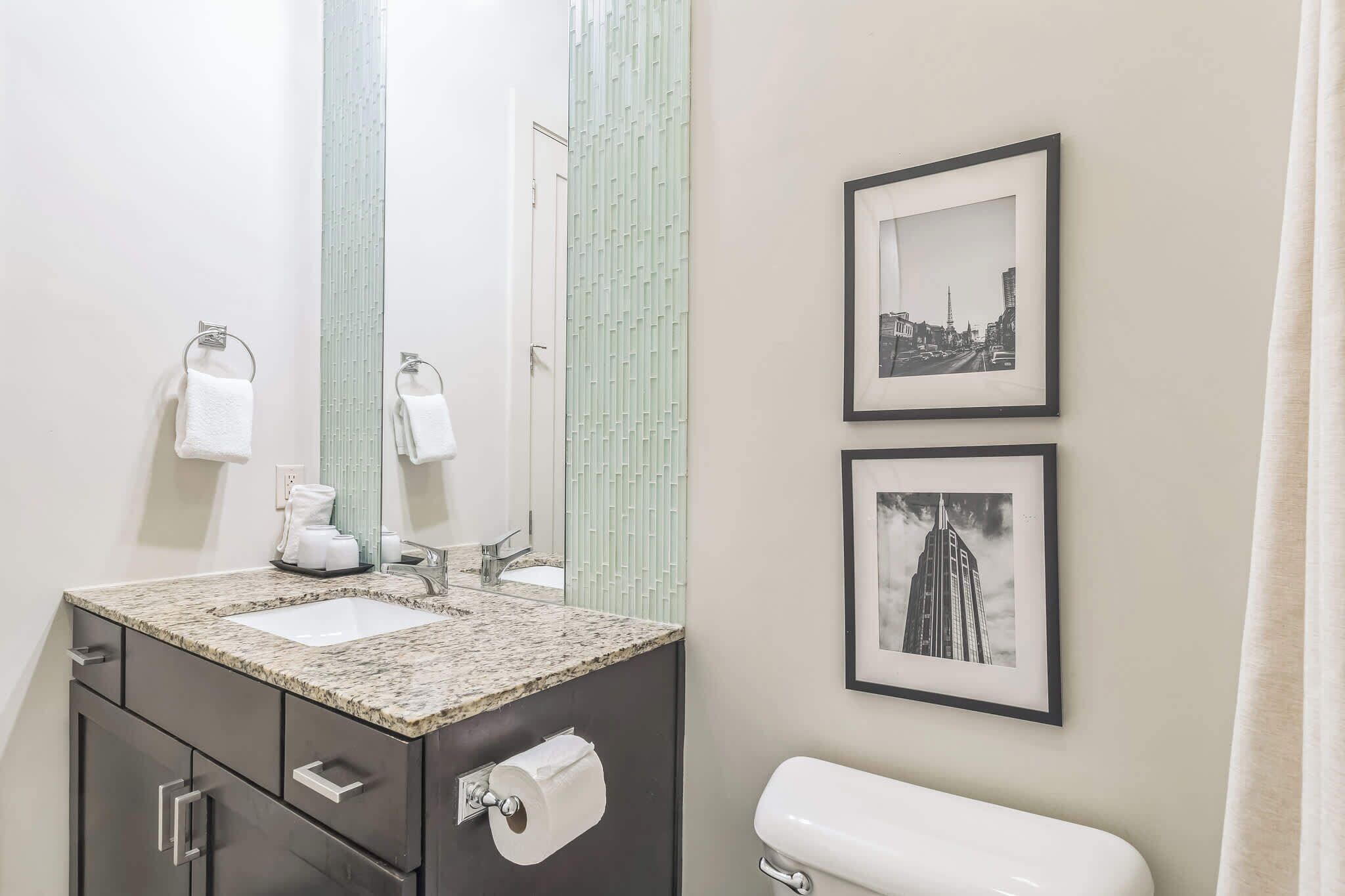 A bathroom with a sink, mirror, toilet, and two framed pictures on the wall.
