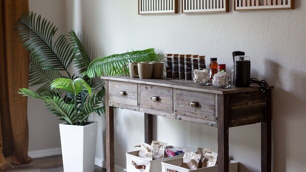 A wooden console table with storage bins, a potted plant, and decorative wall art. - Bright & Bold Retreat in Tulsa, OK (Tulsa)