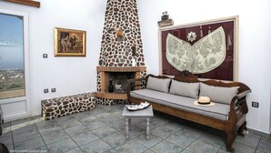 A living room with a stone fireplace, a sofa, a bench, and a painting on the wall. - Villa Anna with Panoramic view (Santorini)