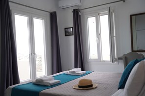 A hotel room with a bed, a window, curtains, a towel rack, and a mirror. - Villa Anna with Panoramic view (Santorini)