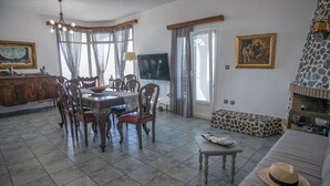 A dining area with a round table and chairs, a television, and a stone fireplace. - Villa Anna with Panoramic view (Santorini)
