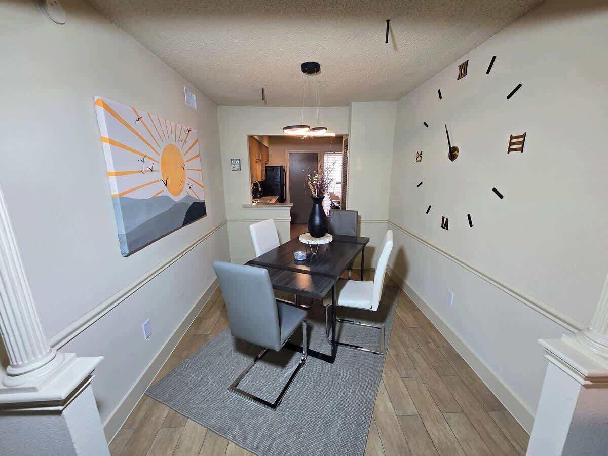 A dining room with a table, chairs, a clock, and a sun painting on the wall.