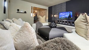 Una sala de estar moderna con sofá, reposapiés y televisor de pantalla plana montado en la pared.