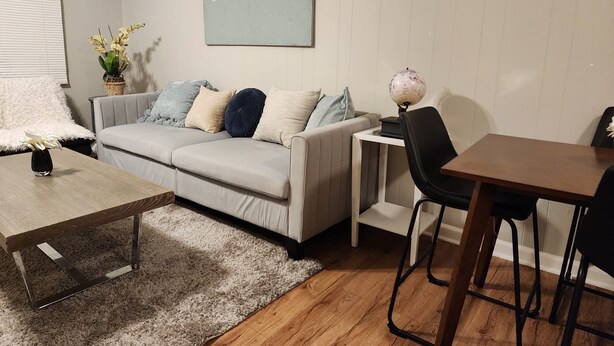 Een moderne woonkamer met een grijze bank, een houten salontafel, een klein bijzettafeltje en een globe lamp.