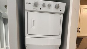 Een compact wit was- en droogapparaat van Whirlpool in een keuken met houten vloeren en lichte wanden.