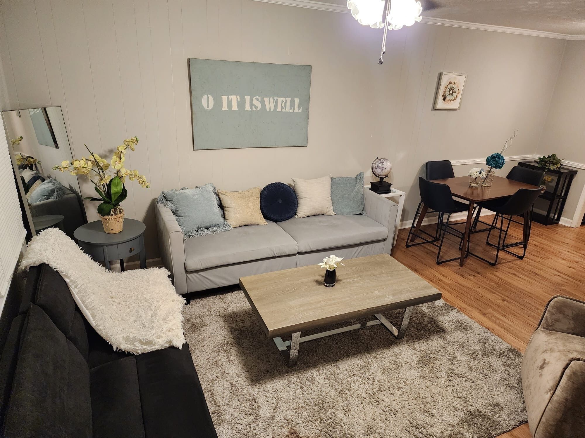 Een woonkamer met een grijze bank, een salontafel en een eethoek met een tafel en stoelen.