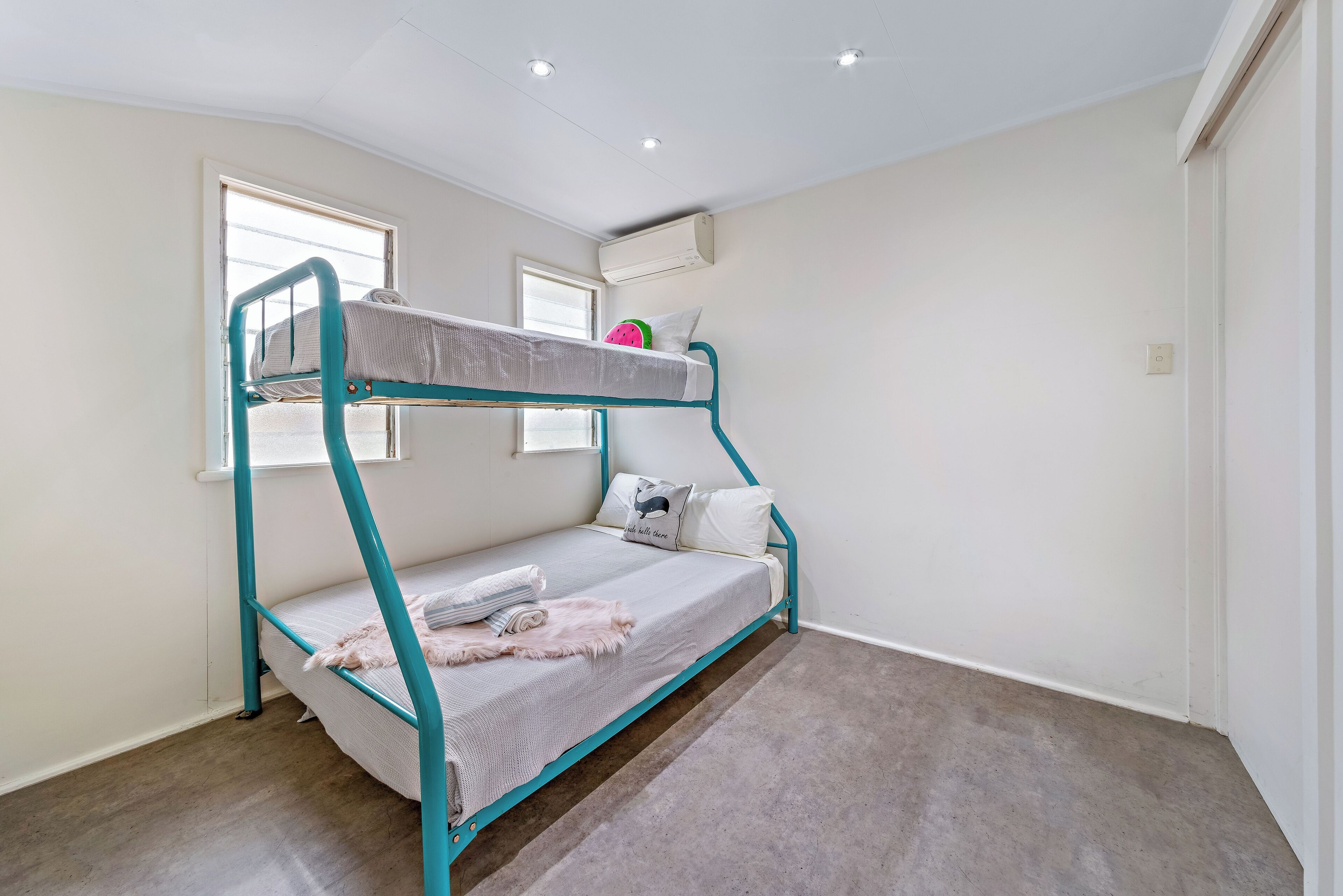 A bunk bed room with a window, air conditioning unit, and a light-colored carpet.
