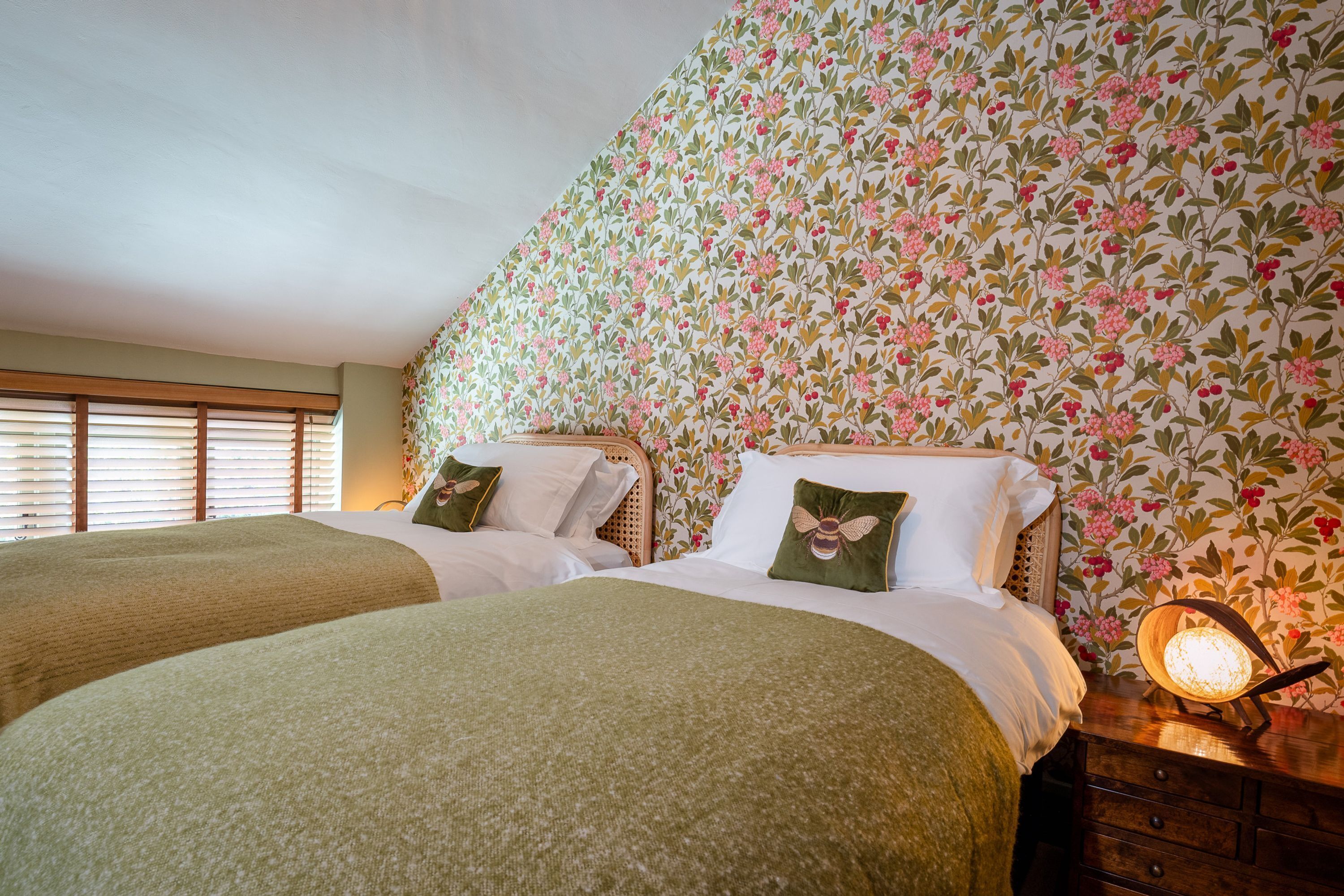 Een kamer met twee bedden, bloemenbehang en een nachtkastje met een lamp.