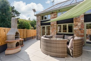 A stone house with a built-in pizza oven, wicker furniture, and a wooden fence. - Woodpeckers in Marldon (Paignton)