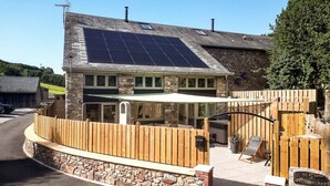 Un bâtiment doté d’une façade en pierre, de panneaux solaires sur le toit et d’une clôture en bois.
