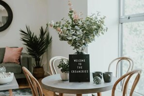 A round dining table with a black sign, a potted plant, and two mugs.