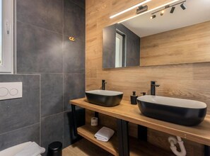 Un baño moderno con dos lavamanos sobre encimera, un mueble de tocador de madera, un espejo y un perchero para toallas.
