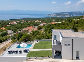 Un edificio moderno con piscina y zona de estar al aire libre, rodeado de vegetación exuberante y vistas al mar.
