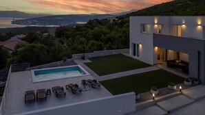 Une maison moderne dotée d’une piscine, d’un espace extérieur aménagé et offrant une vue sur la mer et les montagnes.