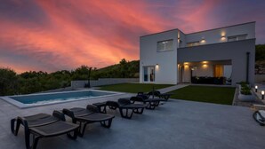 Une maison moderne dotée d’une piscine, d’un espace salon extérieur et offrant une vue sur un ciel au coucher du soleil.