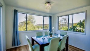 A dining room with a table set for six, large windows with a view of trees and hills, and a chandelier.