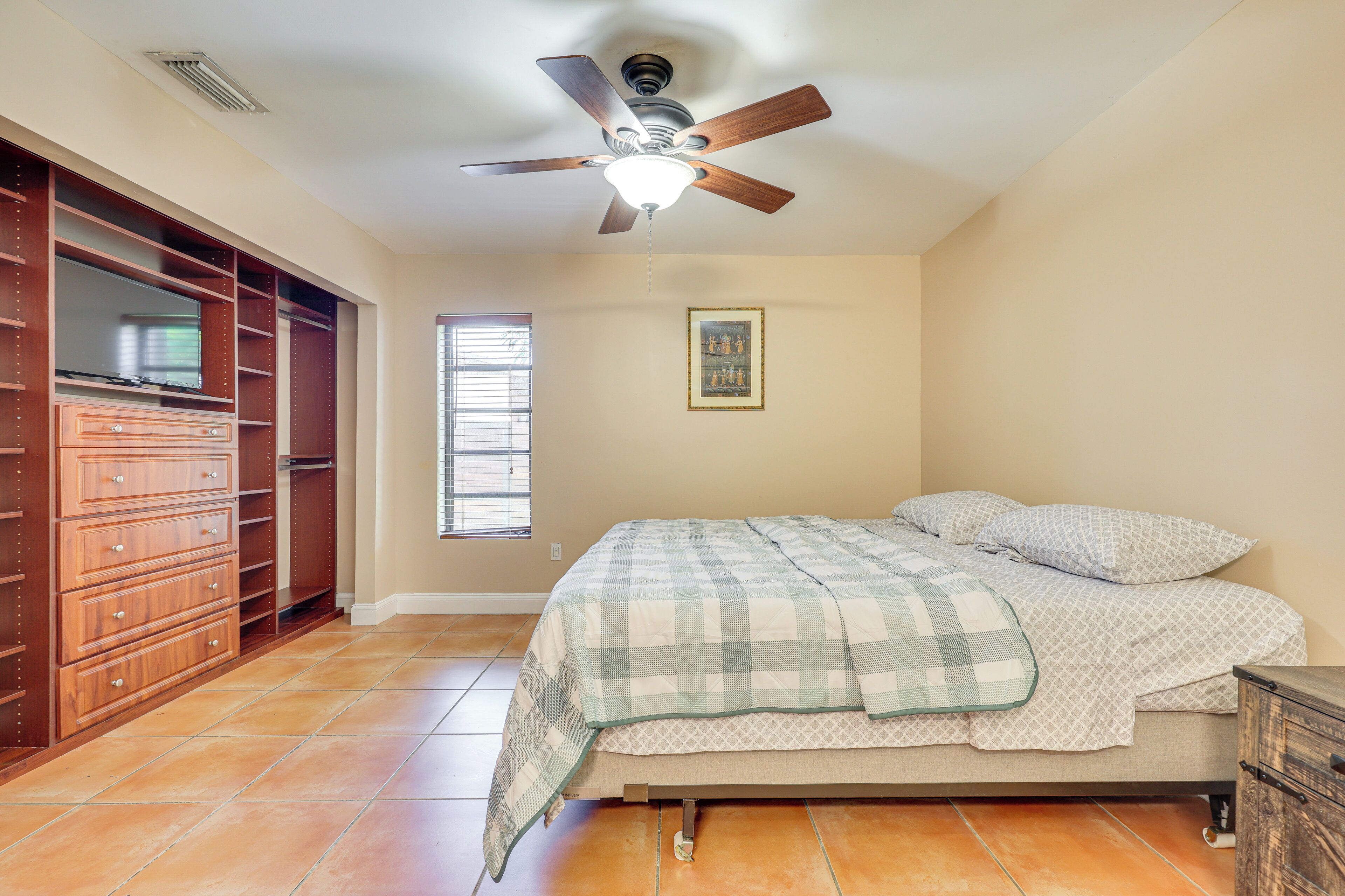 A bedroom with a bed, wooden dresser, closet, and a ceiling fan.
