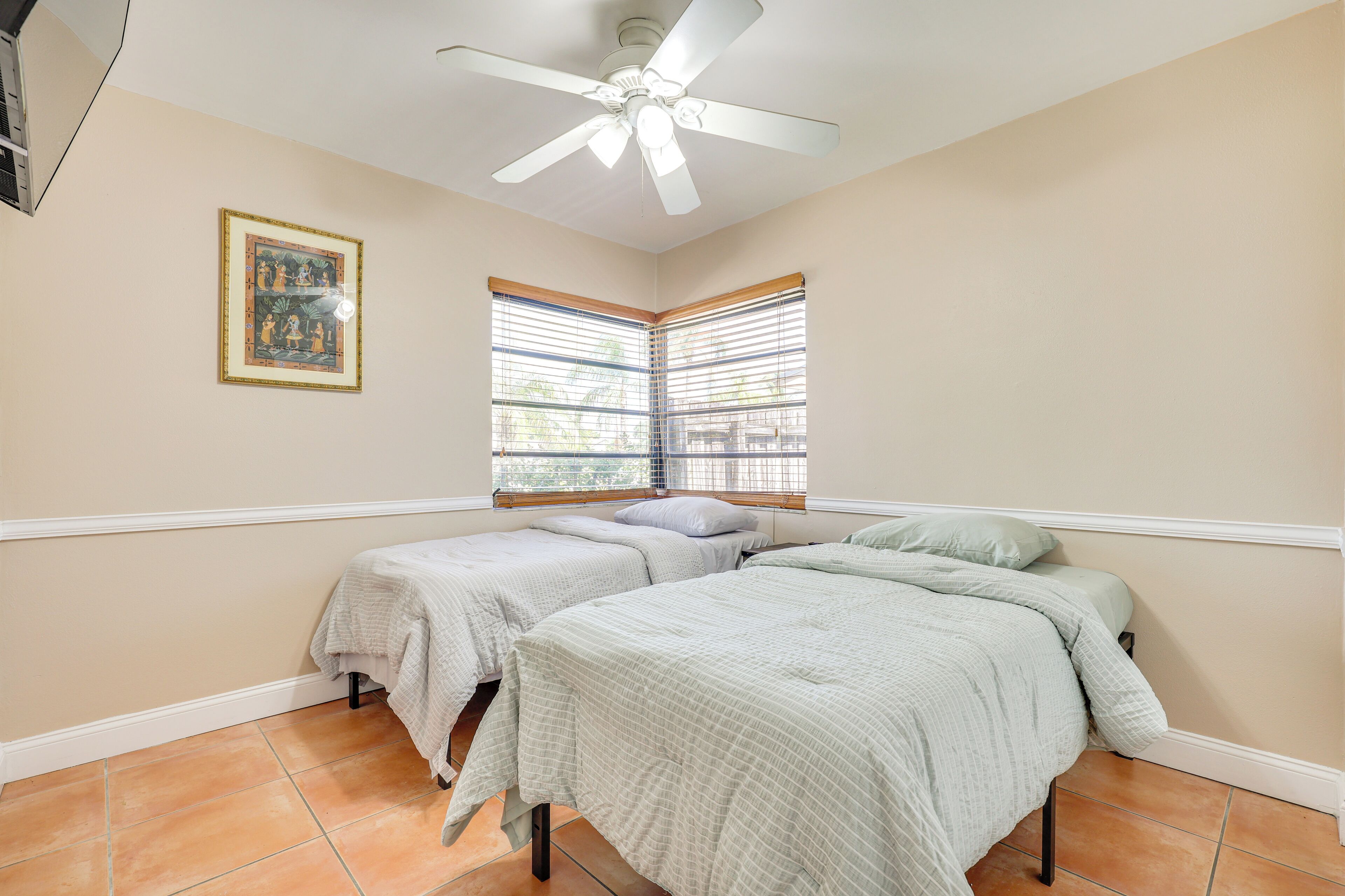 A bedroom with two single beds, a ceiling fan, and a window with blinds.