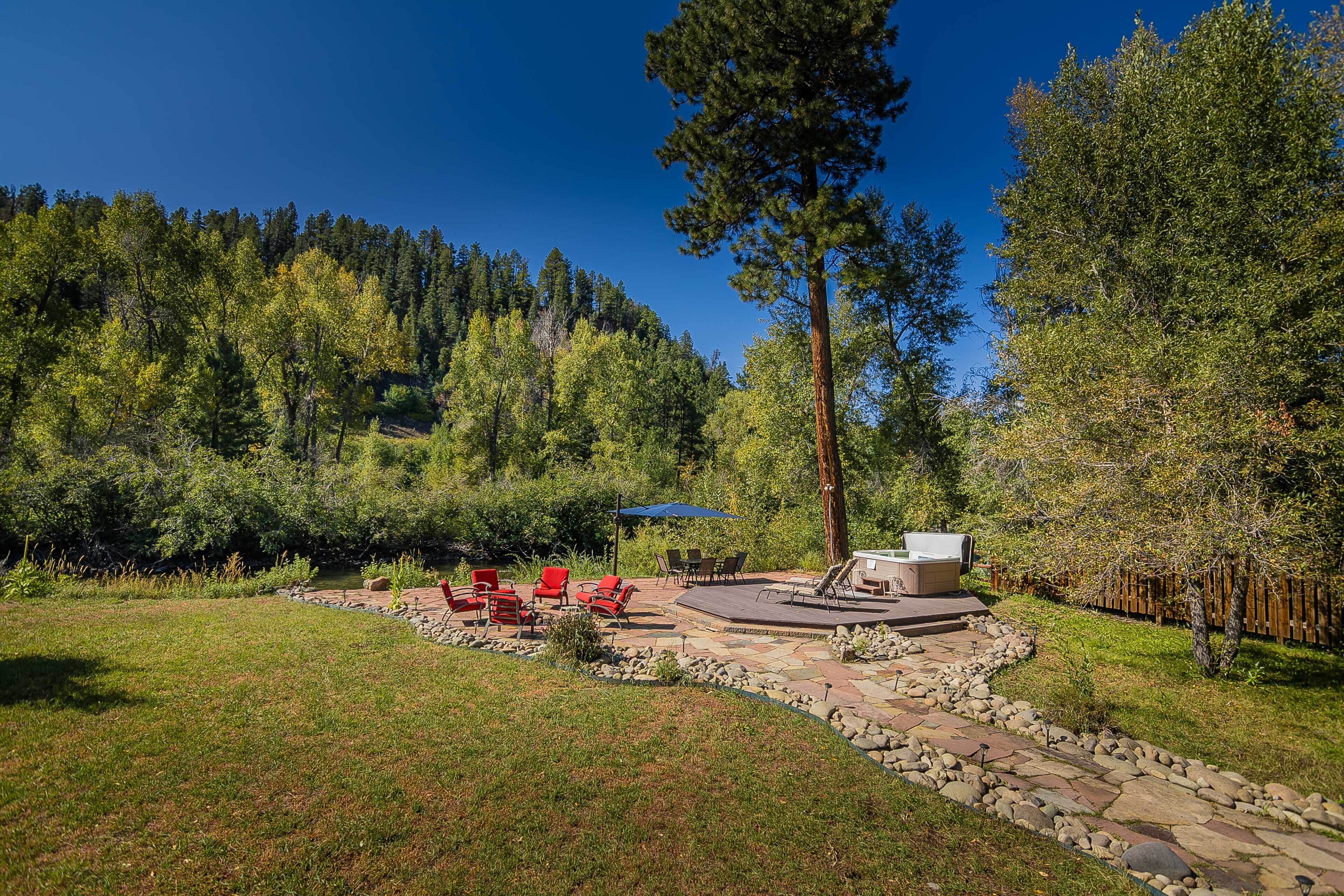 A backyard with a stone patio, outdoor seating, and a barbecue area surrounded by trees.
