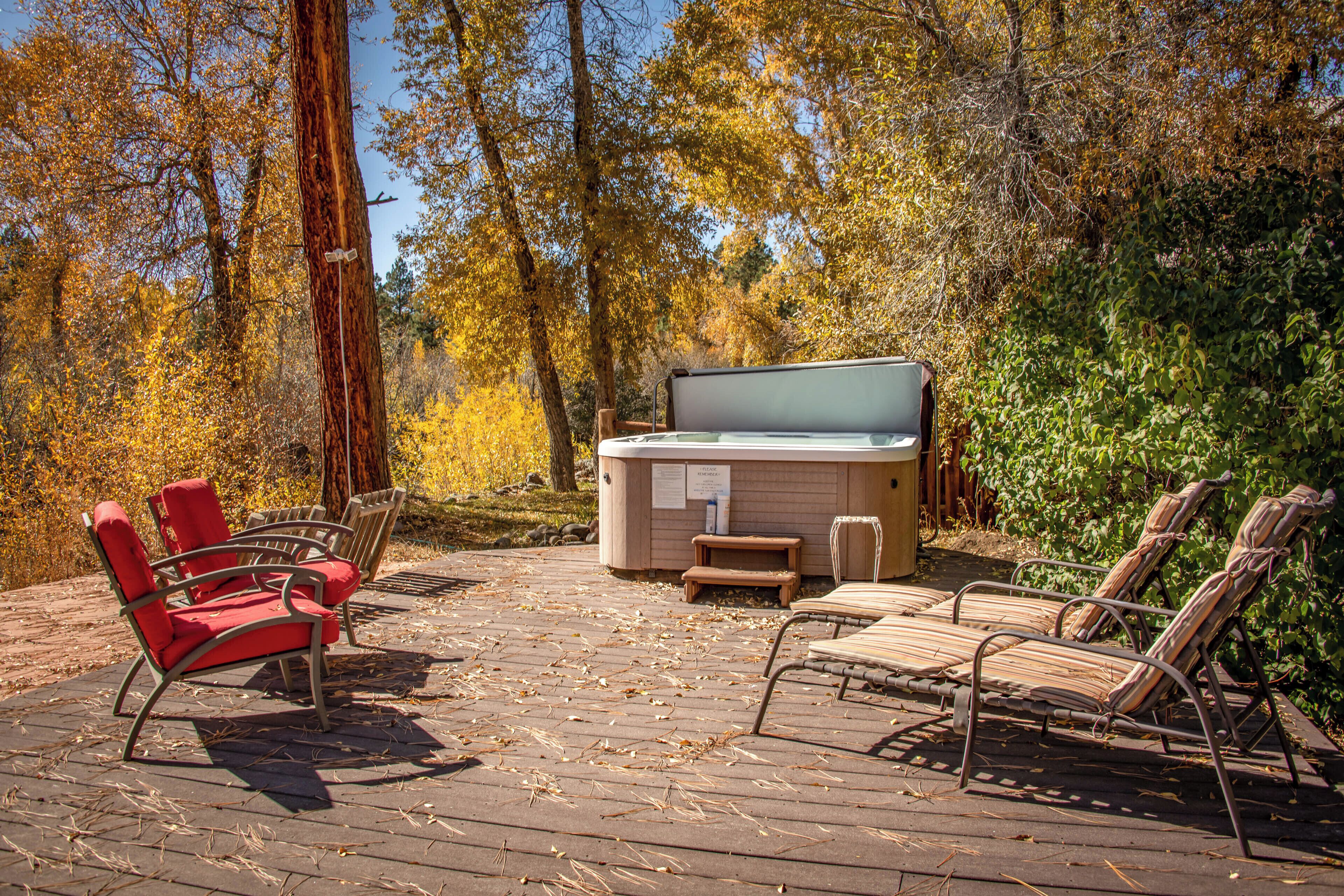 An outdoor patio with a hot tub, lounge chairs, and a wooden table.