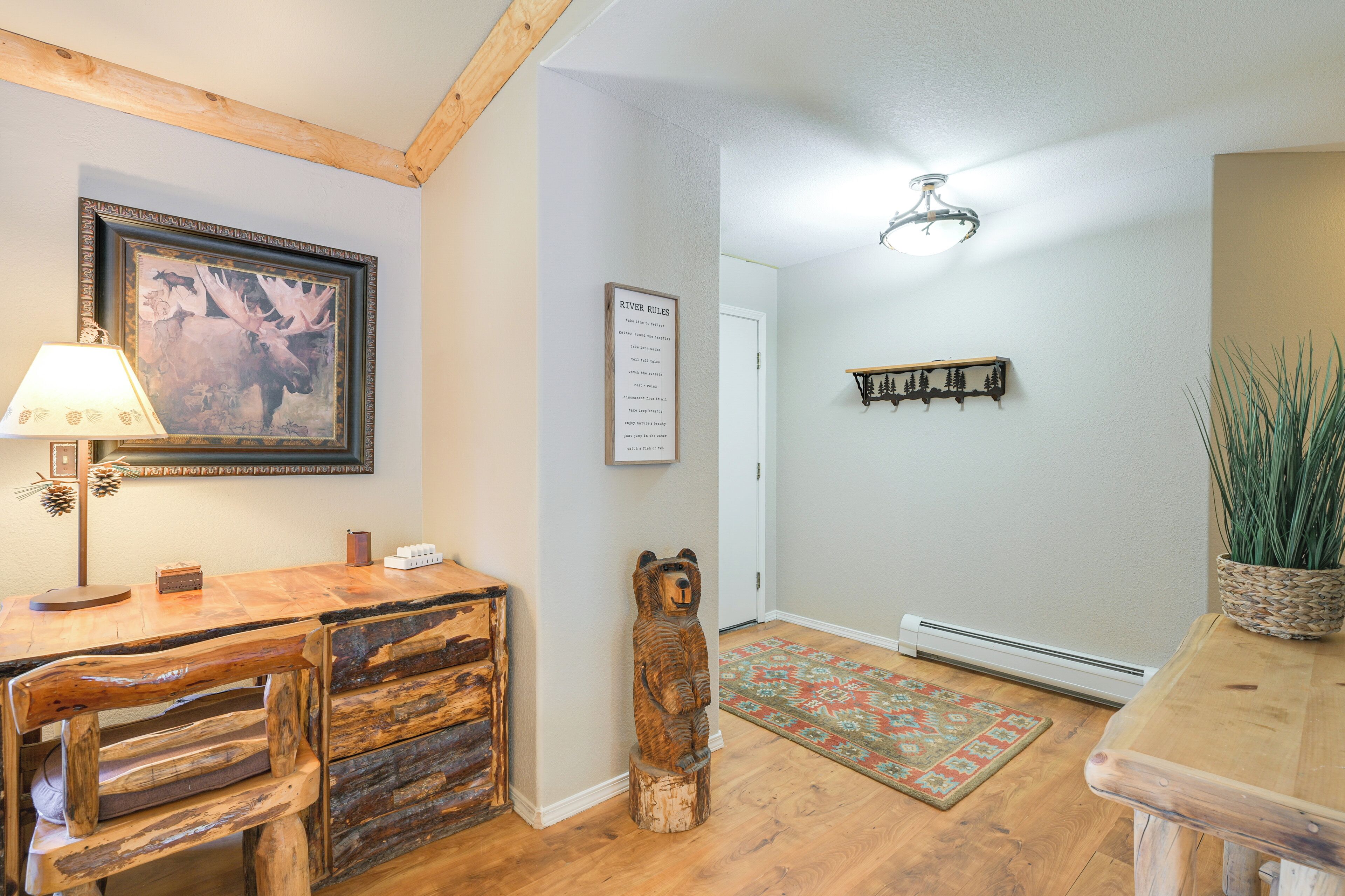 A wooden desk with a lamp, a framed moose picture, a bear sculpture, and a rug.