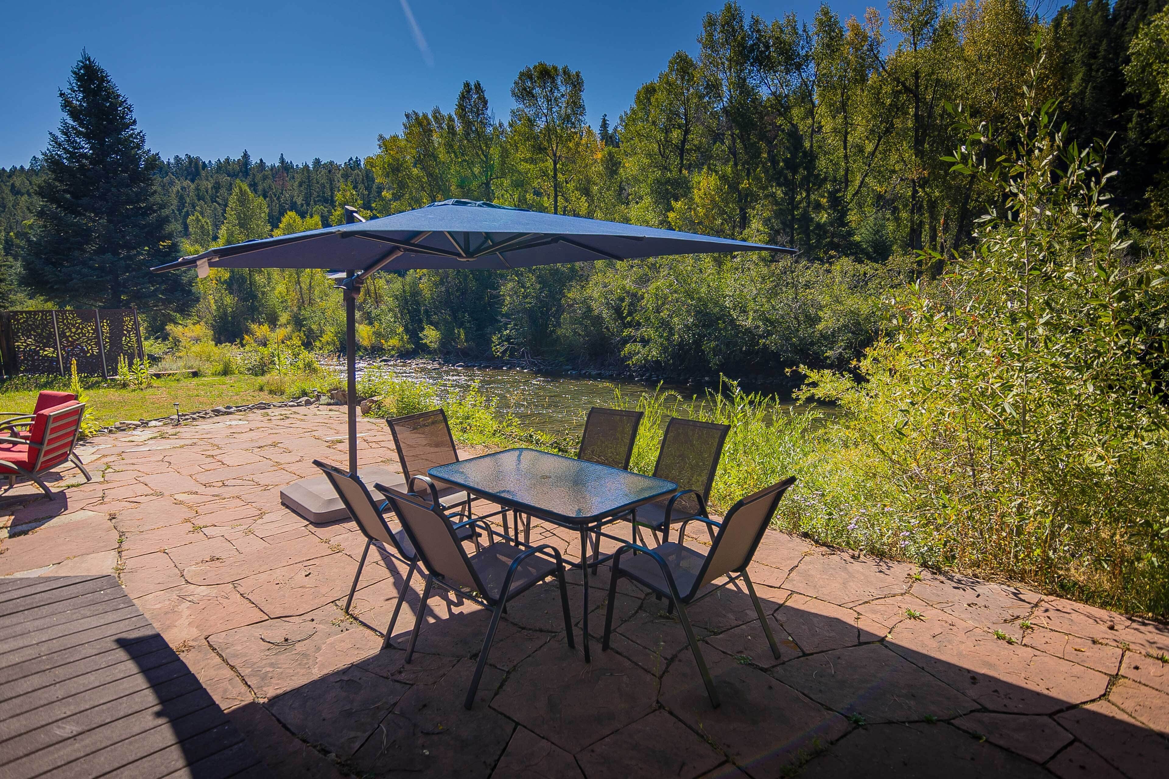 An outdoor patio with a table and chairs, a large umbrella, and a river view.