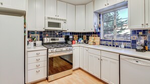 Una cucina con mobili bianchi, un fornello, un forno a microonde e una finestra vista alberi.