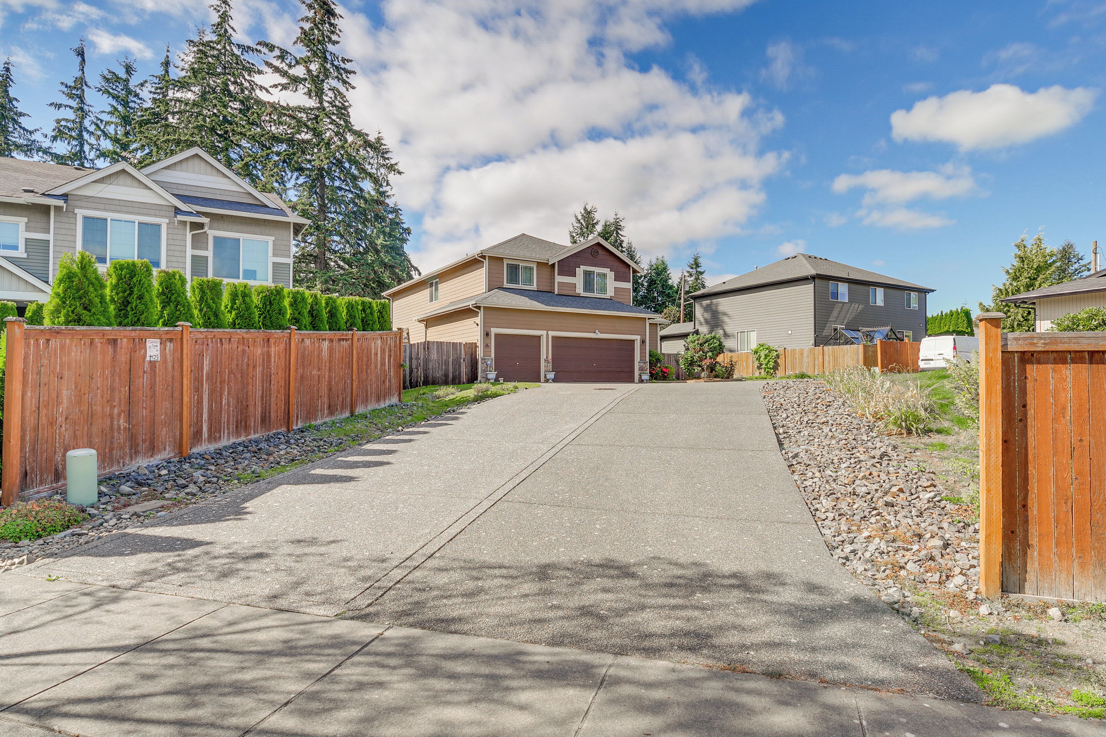 A residential street with houses, a concrete driveway, and a wooden fence.