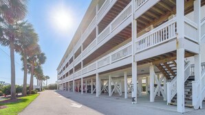 A multi-story building with a covered parking area and a staircase leading to the upper floors. - Walk to Beach: Family-friendly Surf City Condo! (Holly Ridge)