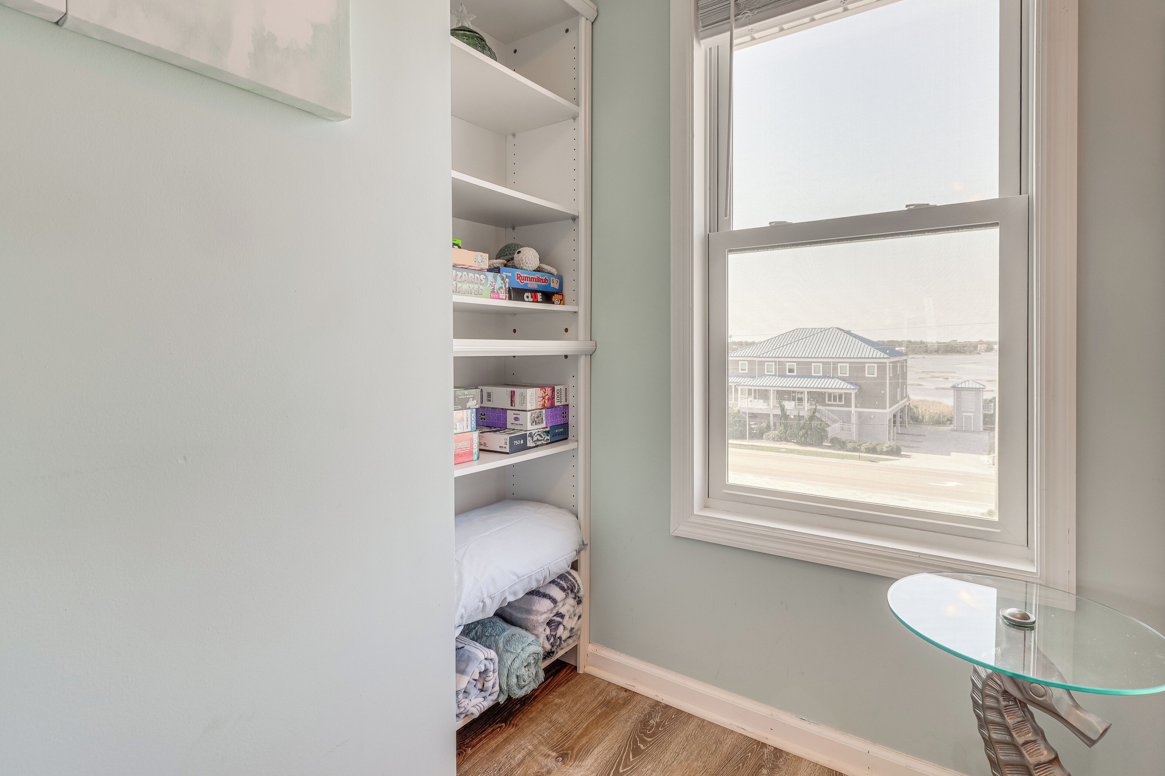 A bedroom with a large window, a glass table, and a closet with shelves.