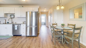 A kitchen with white cabinets, a stainless steel refrigerator, and a wooden dining table with chairs. - Walk to Beach: Family-friendly Surf City Condo! (Holly Ridge)