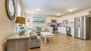A modern kitchen with white cabinets, stainless steel appliances, and a wooden dining table. - Walk to Beach: Family-friendly Surf City Condo! (Holly Ridge)