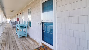 A covered wooden deck with a row of light blue chairs and tables, a blue door, and a white exterior wall. - Walk to Beach: Family-friendly Surf City Condo! (Holly Ridge)