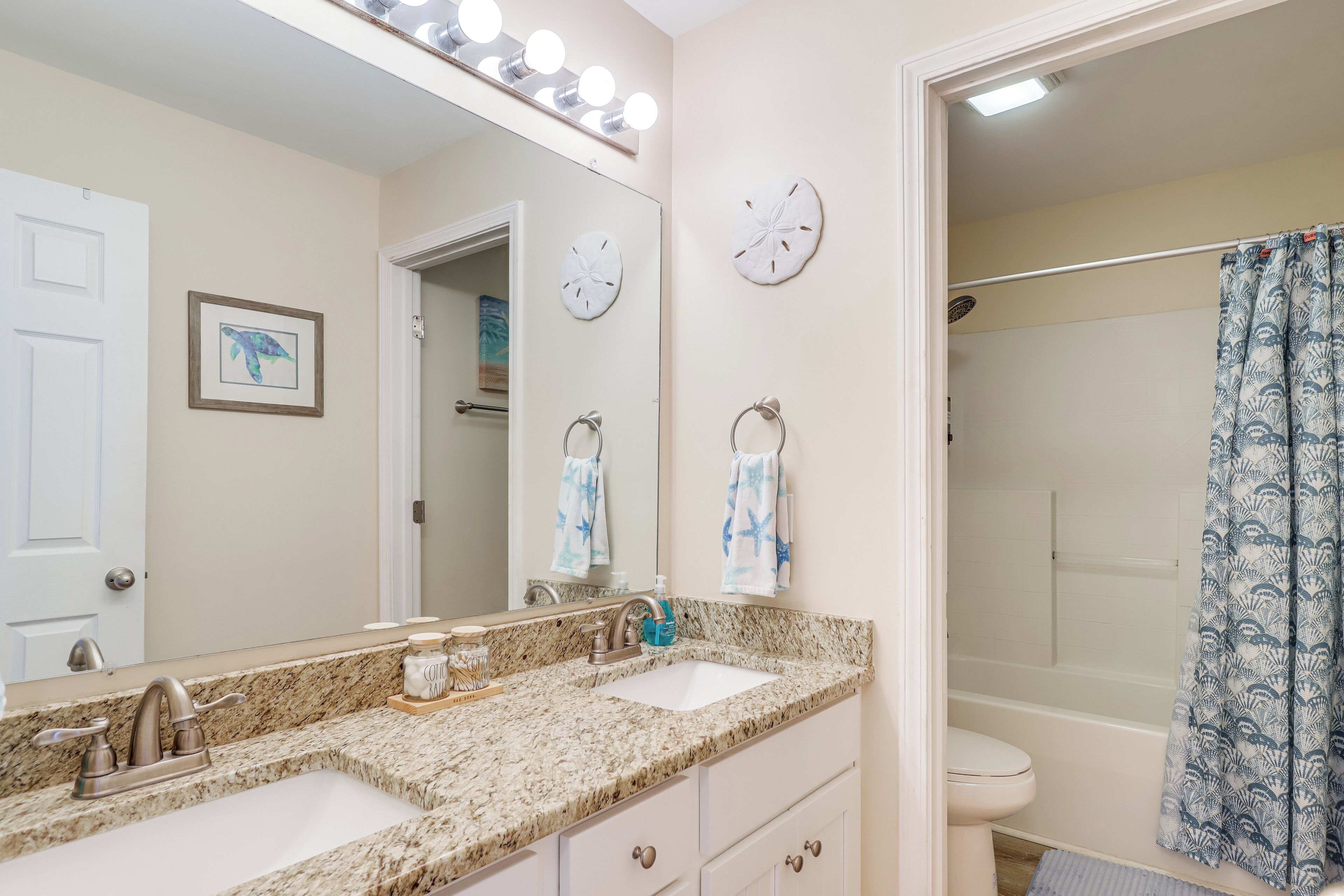 A bathroom with two sinks, a mirror with lights, a clock, and a shower curtain.