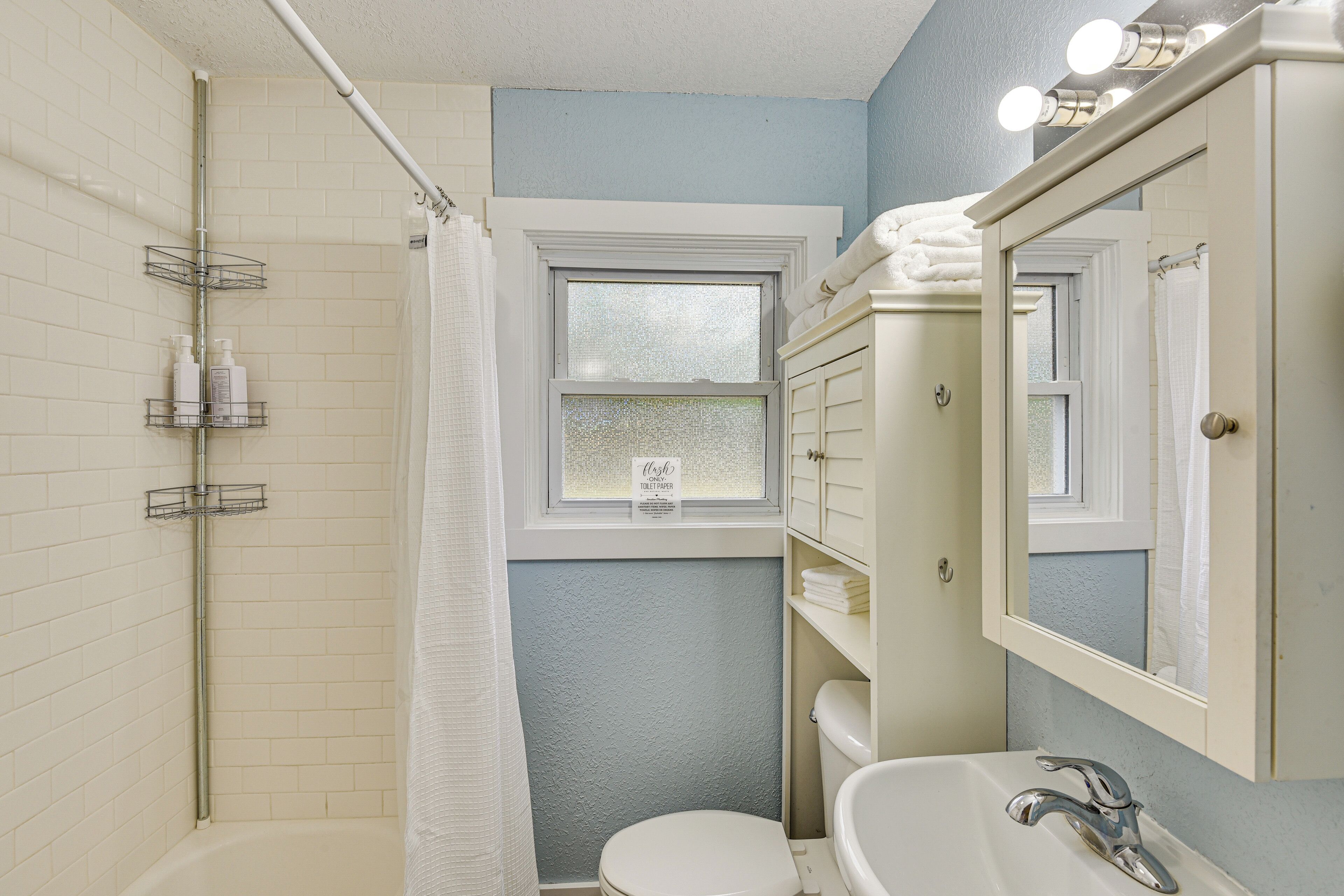 A bathroom with a shower, toilet, sink, and a window with a frosted glass.