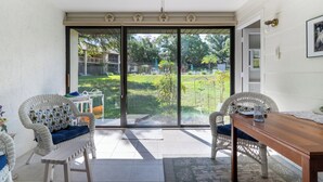 A room with a sliding glass door leading to a garden, wicker furniture, and a wooden table. - Walk to Citrus Hills Golf Club: Condo w/ Pool! (Hernando)