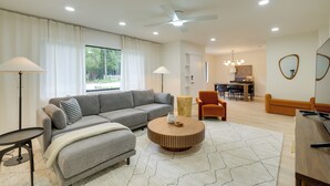 Un salon moderne avec un canapé gris, une table basse ronde et un coin repas comprenant une table en bois et des chaises orange.