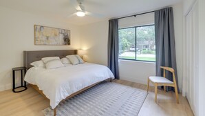 Une chambre à coucher avec un lit, une chaise, un ventilateur de plafond, une fenêtre avec des rideaux et un tableau accroché au mur.